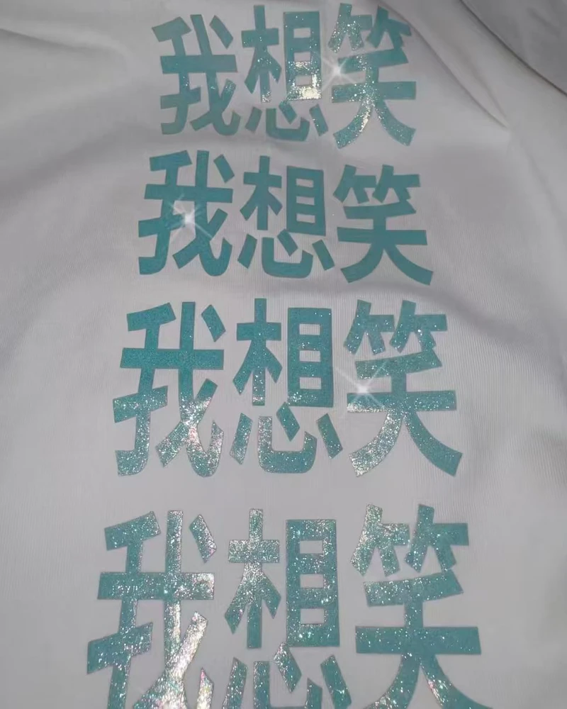 Close-up of glitter turquoise Chinese text meaning I want to laugh on white fabric